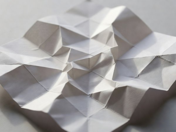 Teilweise eingefallene Miura-Faltung aus weißem Papier mit ihren zickzackförmigen Parallelogramm-Falzlinien
